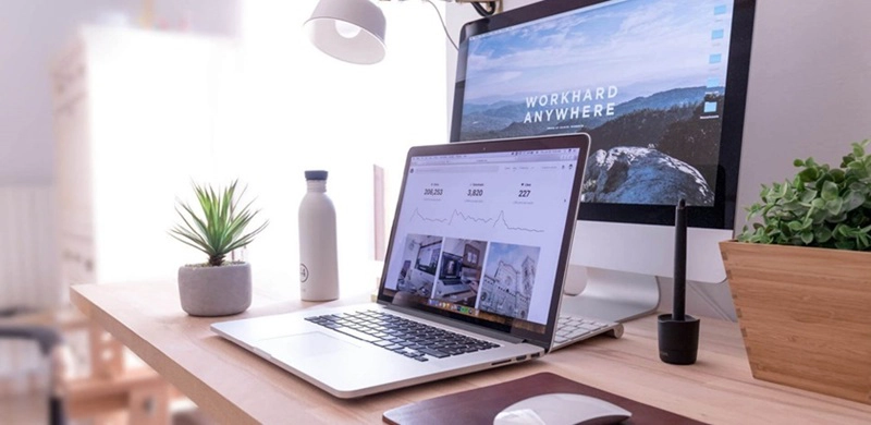 Desktop mit LCD-Monitor und zusätzlichem Notebook jeweils mit Wallpaper Bild. Auf dem Desktop stehen zwei Blumenvasen mit Pflanzen